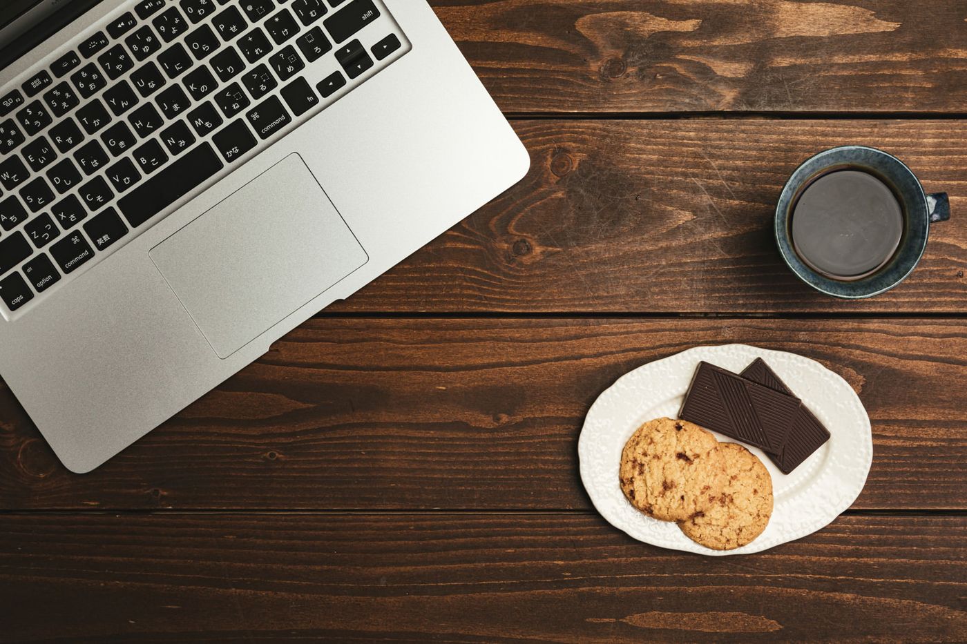 ノートパソコンの横に置かれたコーヒーとクッキー